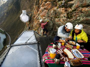 Guests have breakfast as another guest climbs to gather at the Skylodge Adventure Suites in the Sacred Valley in Cuzco, Peru, August 14, 2015. Tourists taking on an arduous climb up the steep cliff face of Peru's Sacred Valley are being rewarded for their efforts by being able to spend the night in transparent mountaintop sleeping pods at the "Skylodge Adventure Suites". To reach the pods, visitors need to climb 400 metres of via ferrata (a steel cable and rungs) up the valley side or hike an intrepid trail through zip lines. Picture taken August 14, 2015. REUTERS/Pilar Olivares  TPX IMAGES OF THE DAY