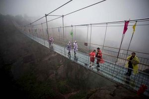 Chinese tourists walk across a glass-bottomed suspension bridge in the Shiniuzhai mountains in Pingjiang county, Hunan province some 150 kilometers from Changsha on October 7, 2015. The bridge, originally a wooden walkway spanning some 300 meters across the 180-meter deep valley, reopened two weeks ago following renovations as a glass-bottomed tourist attraction. AFP PHOTO / JOHANNES EISELE