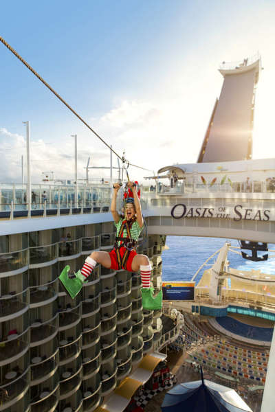 Oasis of the Seas, holiday, man dressed as Santa''s elf in green and red riding ship zipline, laughing, smiling, action, fun, Oasis of the Seas signage in background, Aqua Theater and balconies, below, sky in background,