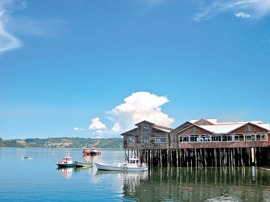 Hut on stilts with blue sky and clear still water, Chiloe, Chile.